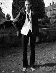 Model standing barefoot in a garden wearing a black blazer, white shirt, and bow tie for Self Service by photographer Stef Mitchell.