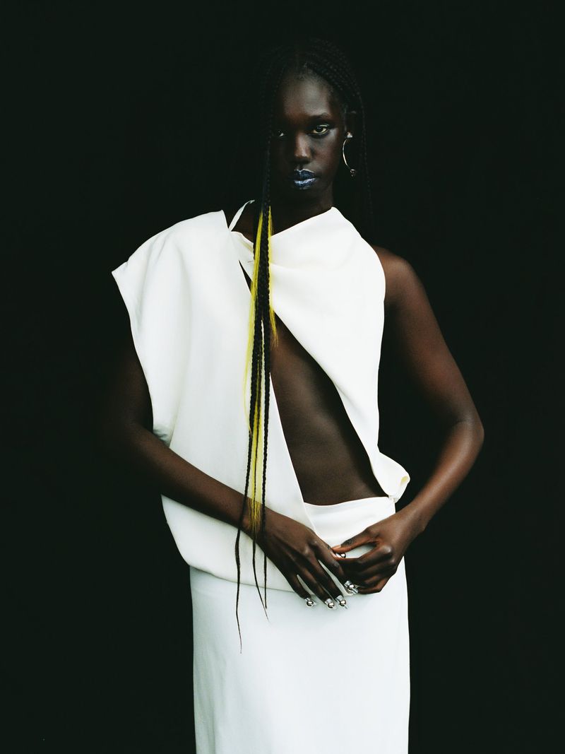 Stunning fashion shot of a Black female model in an elegant white dress against a dark background, showcasing modern high-fashion design.