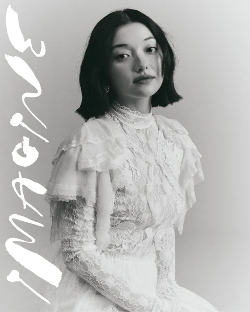 Portrait of an adult female wearing a frilly white lace dress, photographed in a studio with a bright and neutral color palette.