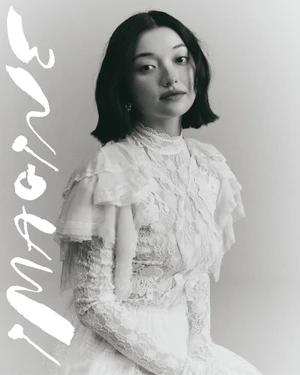 Portrait of a woman wearing a white lace dress with high collar against a light seamless background