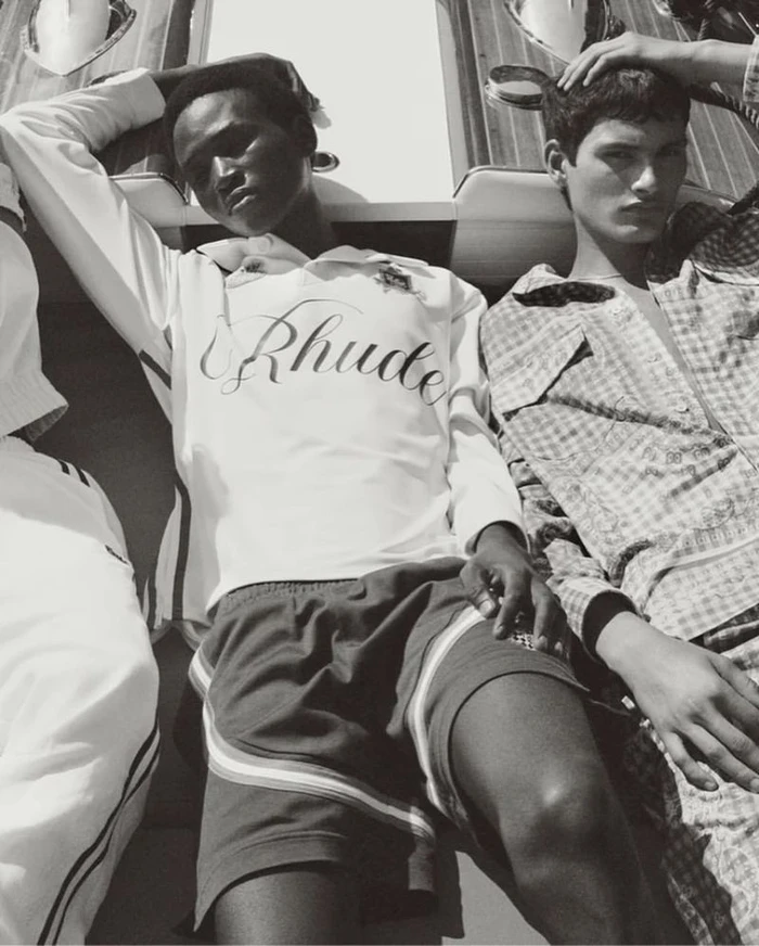 Black and white editorial fashion photograph of male models reclining near a boat for Rhude High Summer 2025.