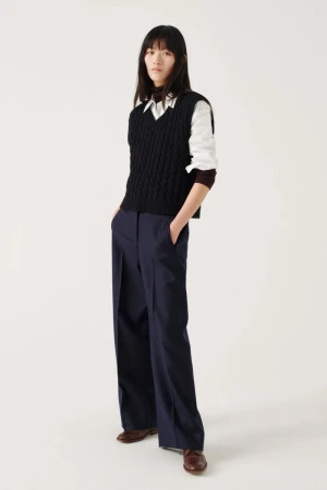 Full-length shot of a young Asian woman in a fashion pose, wearing a cable-knit sweater vest, white shirt, navy pants, and brown leather shoes.