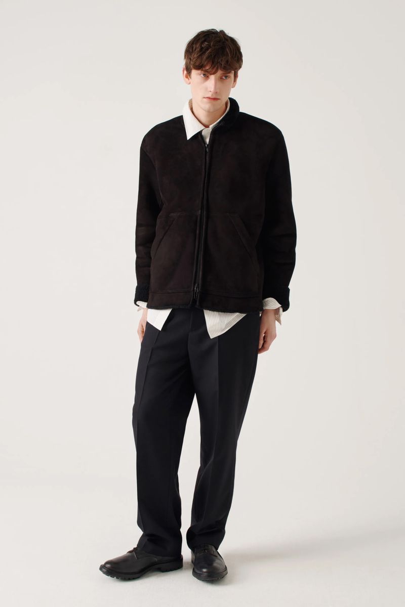 Male model in black jacket and trousers posing in a photo studio with a white background, fashion editorial style, full length studio shot.