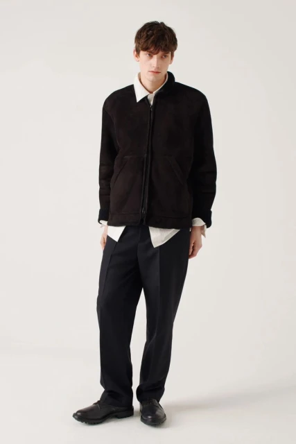 Male model in black jacket and trousers posing in a photo studio with a white background, fashion editorial style, full length studio shot.