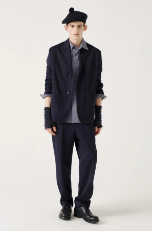 Full-length studio shot of a young adult man in a blazer, shirt, trousers, beret, fingerless gloves and leather shoes, on a white backdrop.