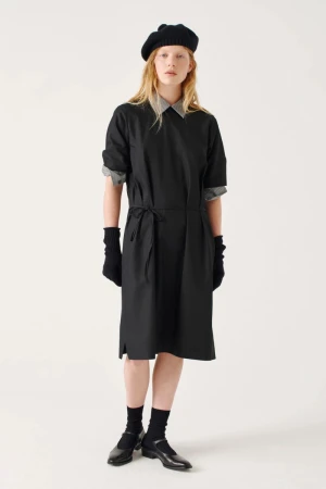Model wearing a black dress over a patterned shirt with a black beret and gloves against a white background