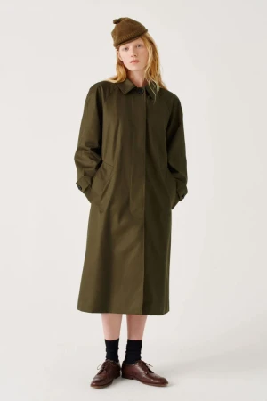 Model wearing an olive green coat and beanie against a seamless white studio background