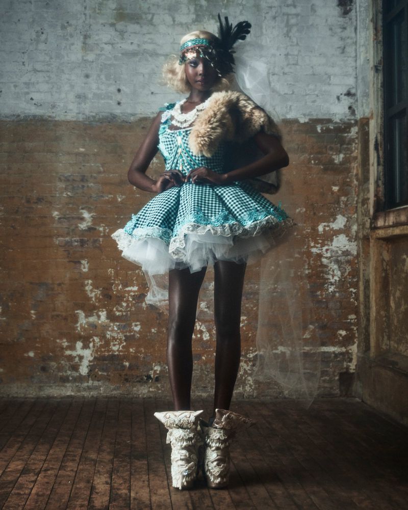Woman in retro-style flapper dress with headpiece poses in room with distressed walls, vintage shoes, and faux fur stole.