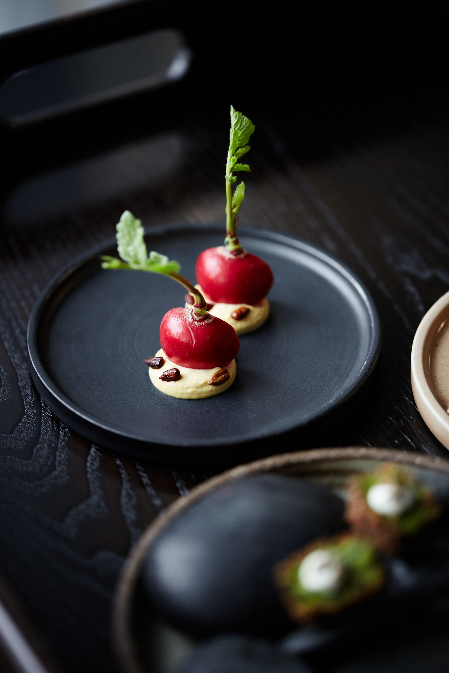 Two hors d'oeuvres, featuring red beet-like globes topped with green sprouts, sit on a small black plate, offering a high-end food presentation.
