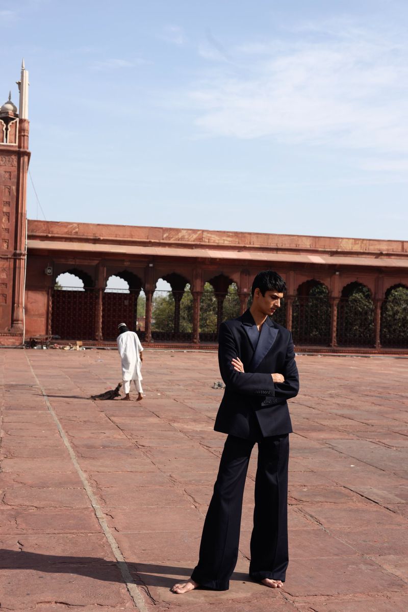 An adult man in a suit stands in the courtyard of Jama Masjid, Delhi, India, with its sandstone structure and minaret in the background.