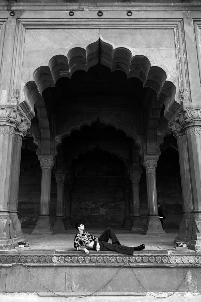 Monochrome portrait of a person lying in an arched alcove with decorative columns. The archway frames the figure.
