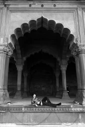 Model lying down inside a historic stone pavilion with ornate arches for Delhi by Les Hommes Publics