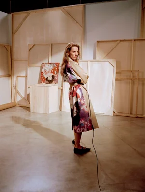 Model in printed coat standing in an art studio with large wooden canvases leaning against the wall