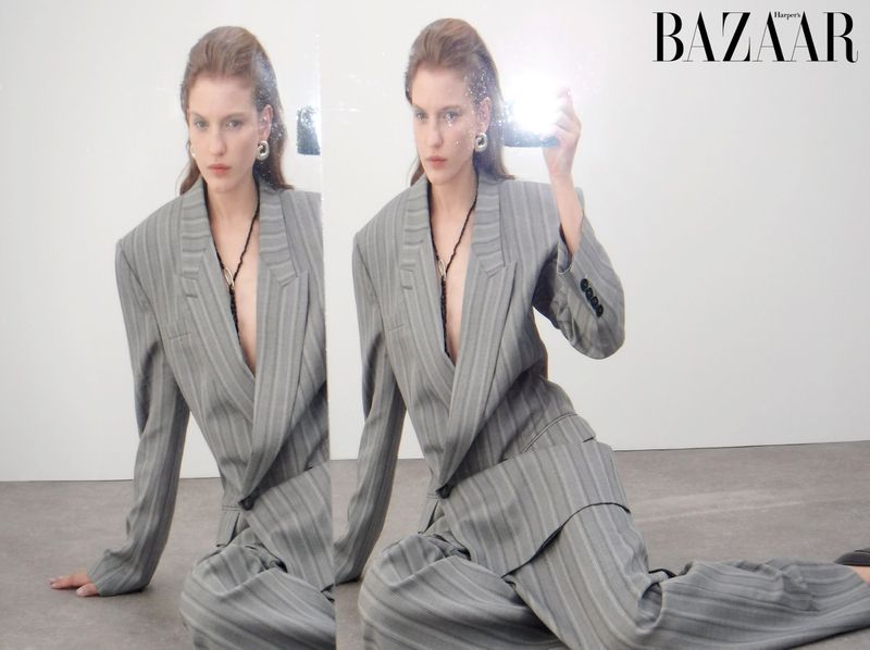 Fashion editorial shot of a woman in a pinstripe suit, posing on the floor with a mirror reflection and Harper's Bazaar logo.