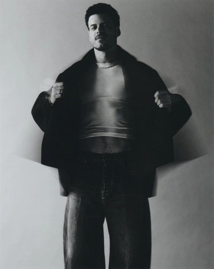 Man wearing a dark coat and light t-shirt with motion blur effect against a plain background