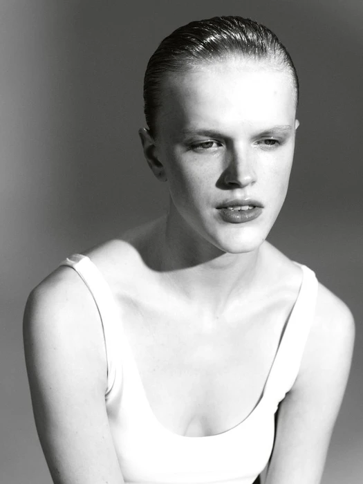 Close-up portrait of model Hannah Motler wearing a white tank top against a neutral grey studio background.