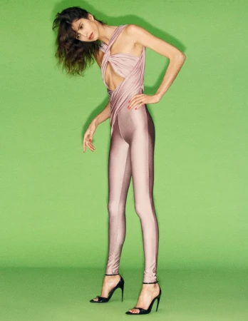 Model Mica Argañaraz wearing a fitted mauve jumpsuit and black heels against a green backdrop