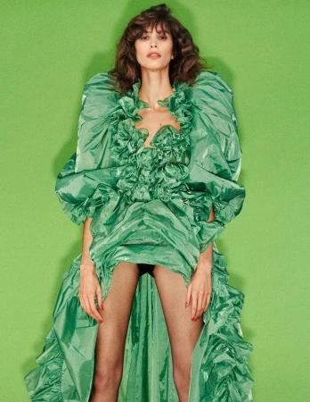 Model Mica Argañaraz wearing a voluminous green ruffled dress against a green backdrop for Self Service magazine editorial.