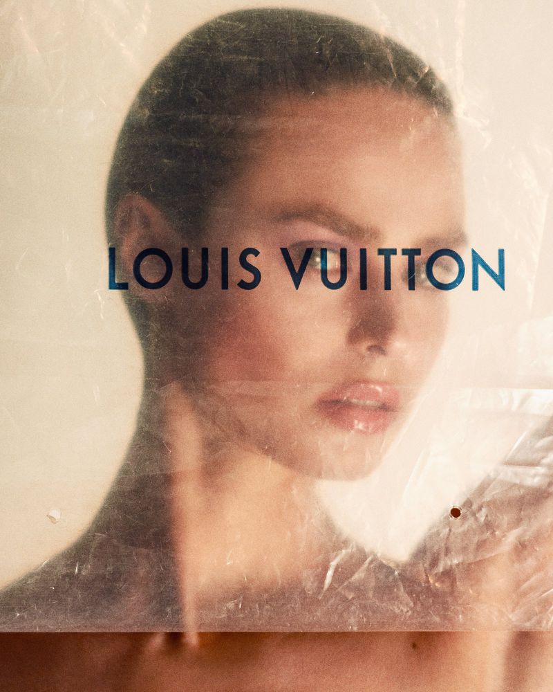 Close-up studio shot of a model posing with the Louis Vuitton logo on a translucent plastic material overlaying her face and upper torso.