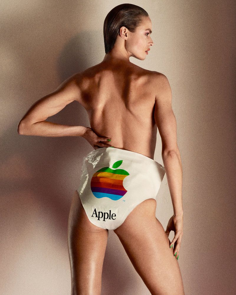 Woman in a photo studio, partially nude, wearing a shopping bag with Apple logo as underwear, showcasing body, shoulders, and head.