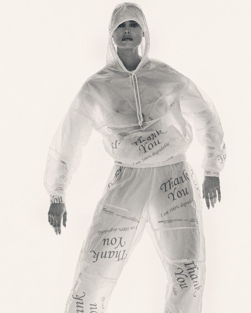 Woman in transparent hooded tracksuit with 'Thank You' text. Full-length shot against a bright white background in a fashion setting.