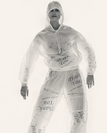 Woman in transparent hooded tracksuit with 'Thank You' text. Full-length shot against a bright white background in a fashion setting.