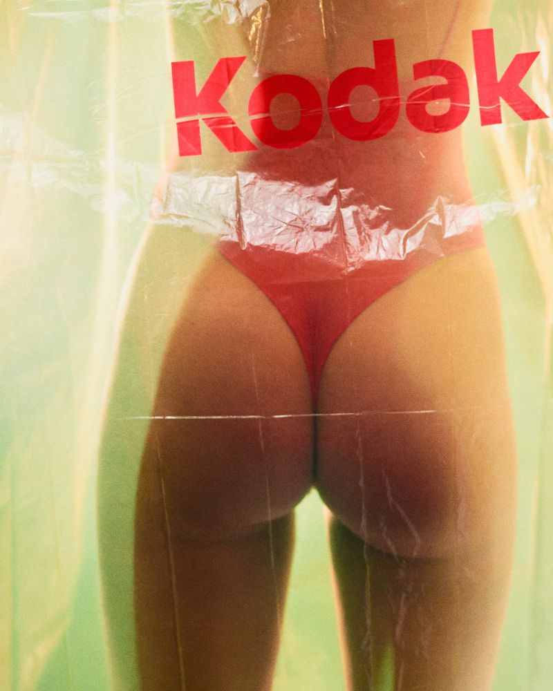 Woman's torso and red bikini bottoms are visible through a translucent plastic bag with a red Kodak logo on a light green background.