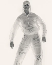 Model Birgit Kos wearing a translucent hooded top and trousers printed with Thank You text on white seamless background.