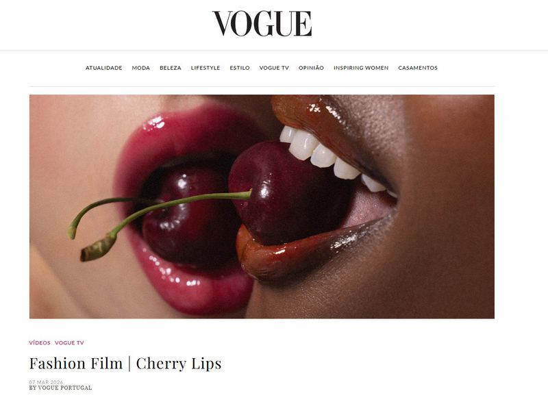 Two models of different ethnicities with glossy cherry lipstick share a cherry in a close-up shot for a Vogue fashion film.