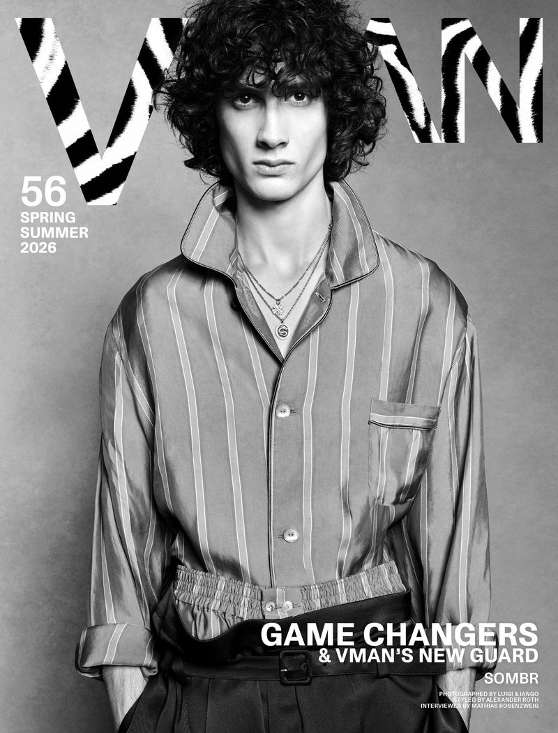 VMAN magazine cover features a young adult male with curly hair, wearing a vertically striped collared shirt, against a grey background.