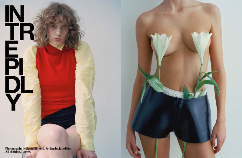 Fashion editorial image: two women in studio lighting, one wearing a bright red top, the other wearing black shorts and holding lilies.
