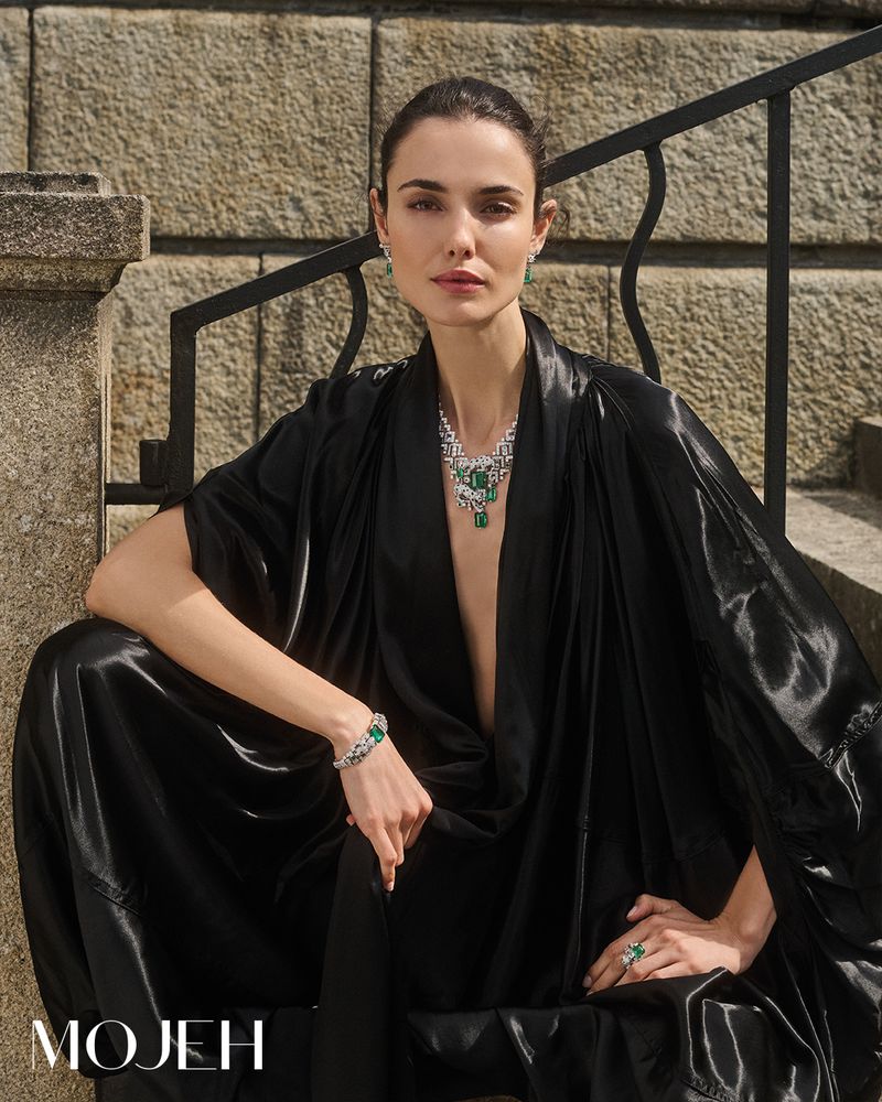 Adult female model in elegant black dress and jewelry sits on stone steps for a fashion and beauty editorial shot in natural light.