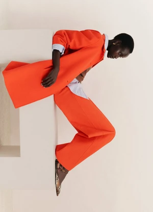 Model Yar Aguer wearing a bright orange coat and trousers against a white background