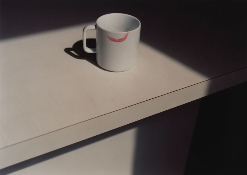 White coffee mug with a visible lipstick stain sits on a white surface, illuminated by natural light and casting shadows.