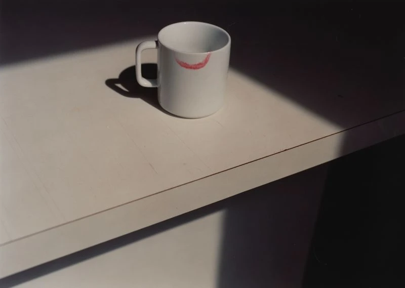 White coffee mug with a visible lipstick stain sits on a white surface, illuminated by natural light and casting shadows.