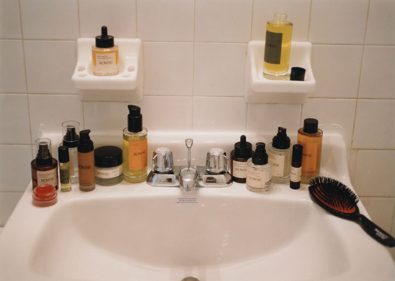 Collection of ROWSE brand skincare products arranged on a white bathroom sink with white tiled backsplash, bright and clean aesthetic.
