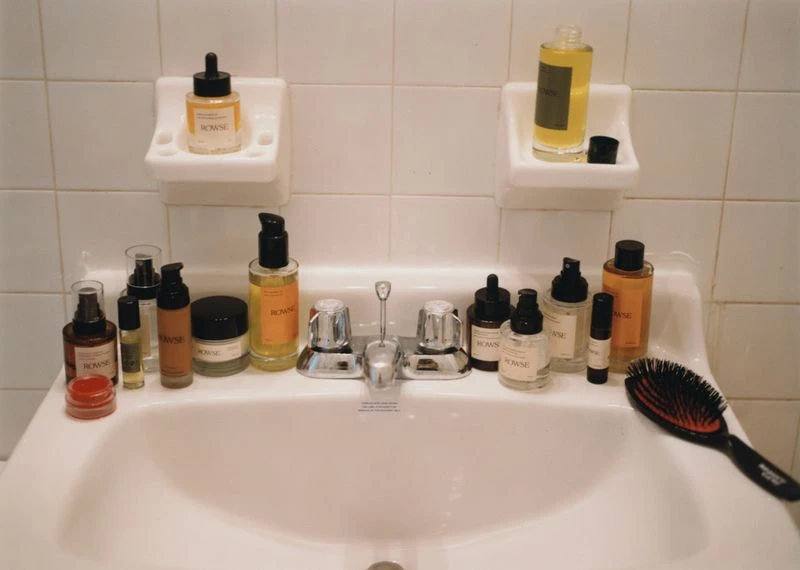 Collection of ROWSE brand skincare products arranged on a white bathroom sink with white tiled backsplash, bright and clean aesthetic.