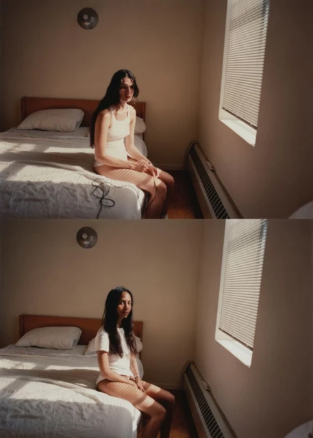 Woman with long dark hair sits on bed near window in indoor bedroom setting with bed, window, and radiator during daytime.