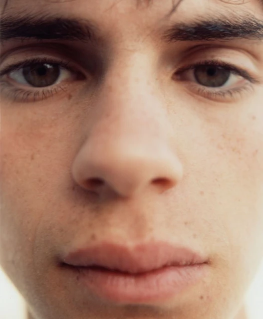 Close-up portrait of a young adult with brown eyes and eyebrows, showing skin details and facial features in soft, natural lighting.