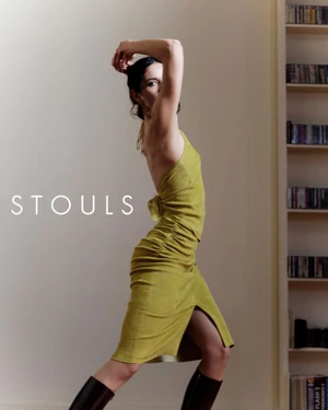 Model in olive green dress and tall boots posing in an interior space with a bookshelf in the background for Stouls Fall Winter 2026