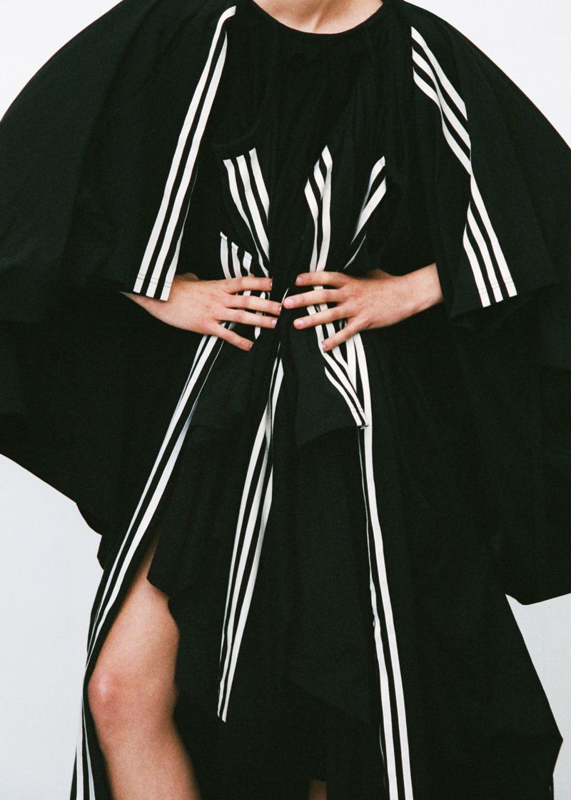 Person in a dramatic black dress with white stripes poses in a studio with hands on waist, fashion photography, elegant and bold.