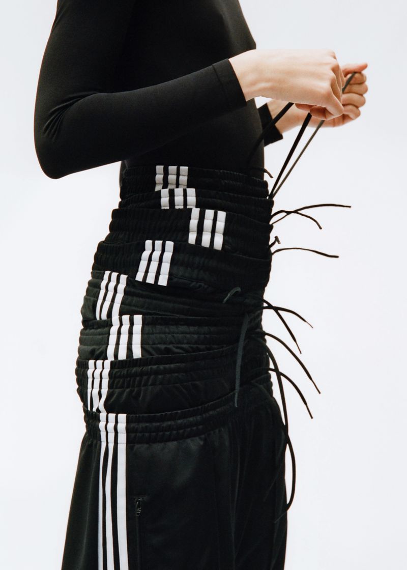 Close-up of a person adjusting the drawstrings on a black Adidas skirt featuring white stripes, against a white background.