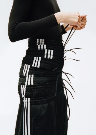 Close-up of a person adjusting the drawstrings on a black Adidas skirt featuring white stripes, against a white background.