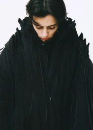 Model wearing a heavy black hooded coat with multiple zippers against a white background