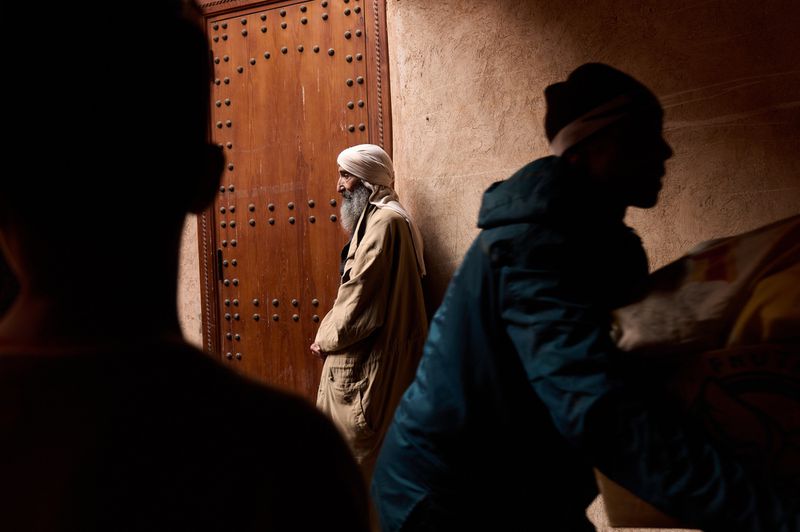 Three men standing near a weathered wooden door in a dimly lit, textured alleyway, creating a sense of depth and intrigue.