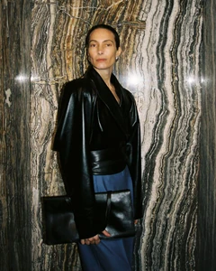 Model Jessica Miller wearing a black leather jacket and holding a black handbag against a polished marble wall for Situationist.