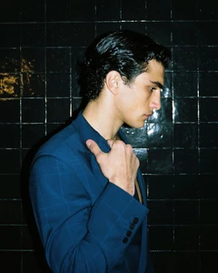 Man wearing a blue blazer adjusting collar against dark glossy tiled background