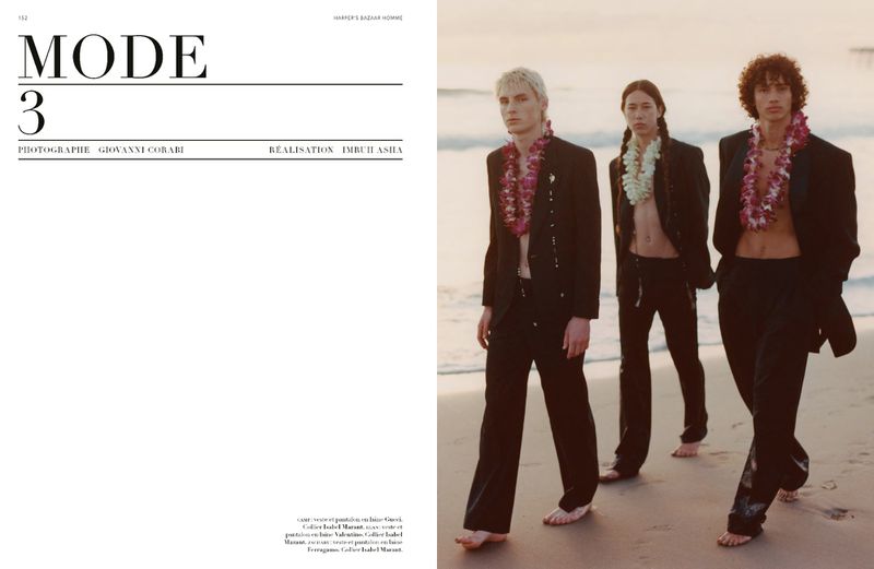 Three male fashion models pose on a beach at dusk wearing dark suits and floral leis for a Harper's Bazaar editorial.