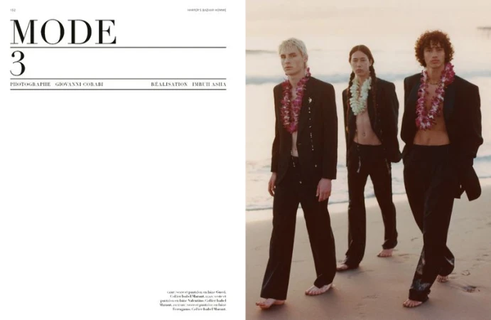 Three male fashion models pose on a beach at dusk wearing dark suits and floral leis for a Harper's Bazaar editorial.