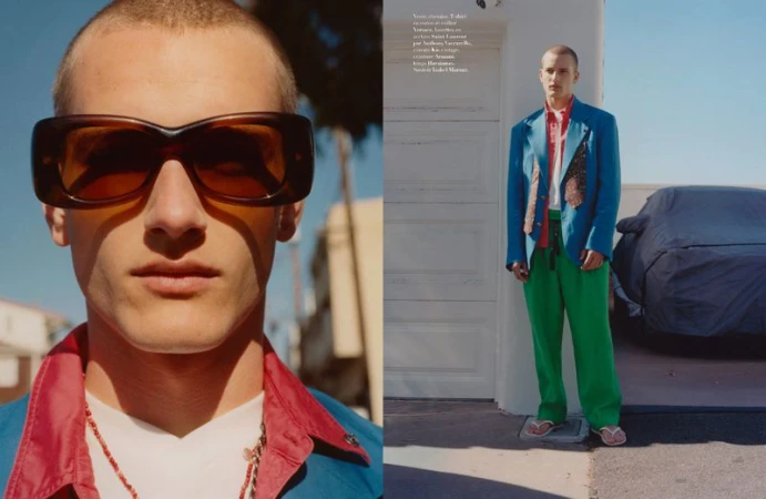 Close-up portrait of a male model wearing oversized brown sunglasses and a blue jacket with a red shirt.